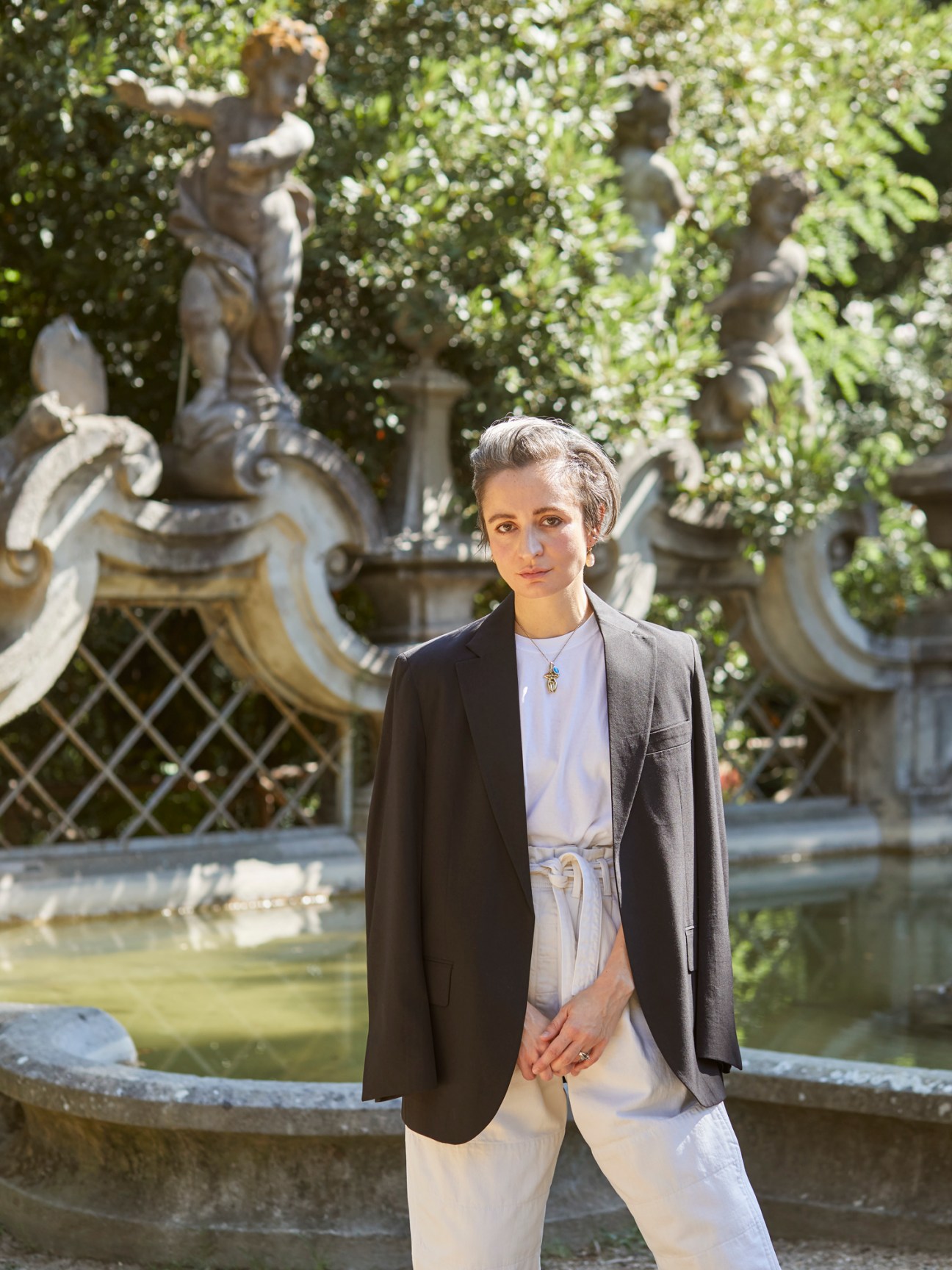 Veronica Leoni, Moncler designer, standing in front of an ornate fountain wearing a dark blazer