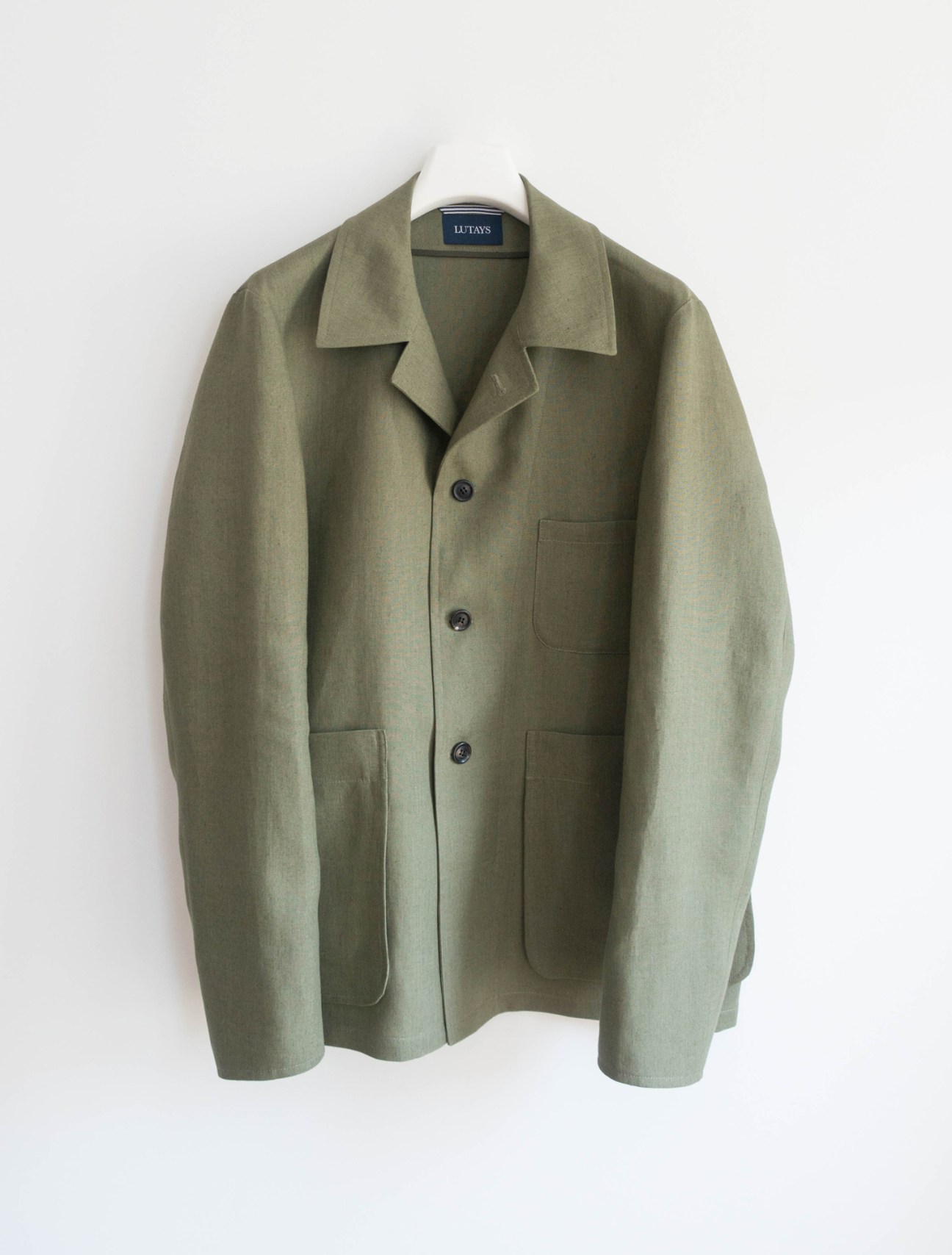 Olive green linen jacket with notched lapels, three buttons, and patch pockets hanging on white hanger