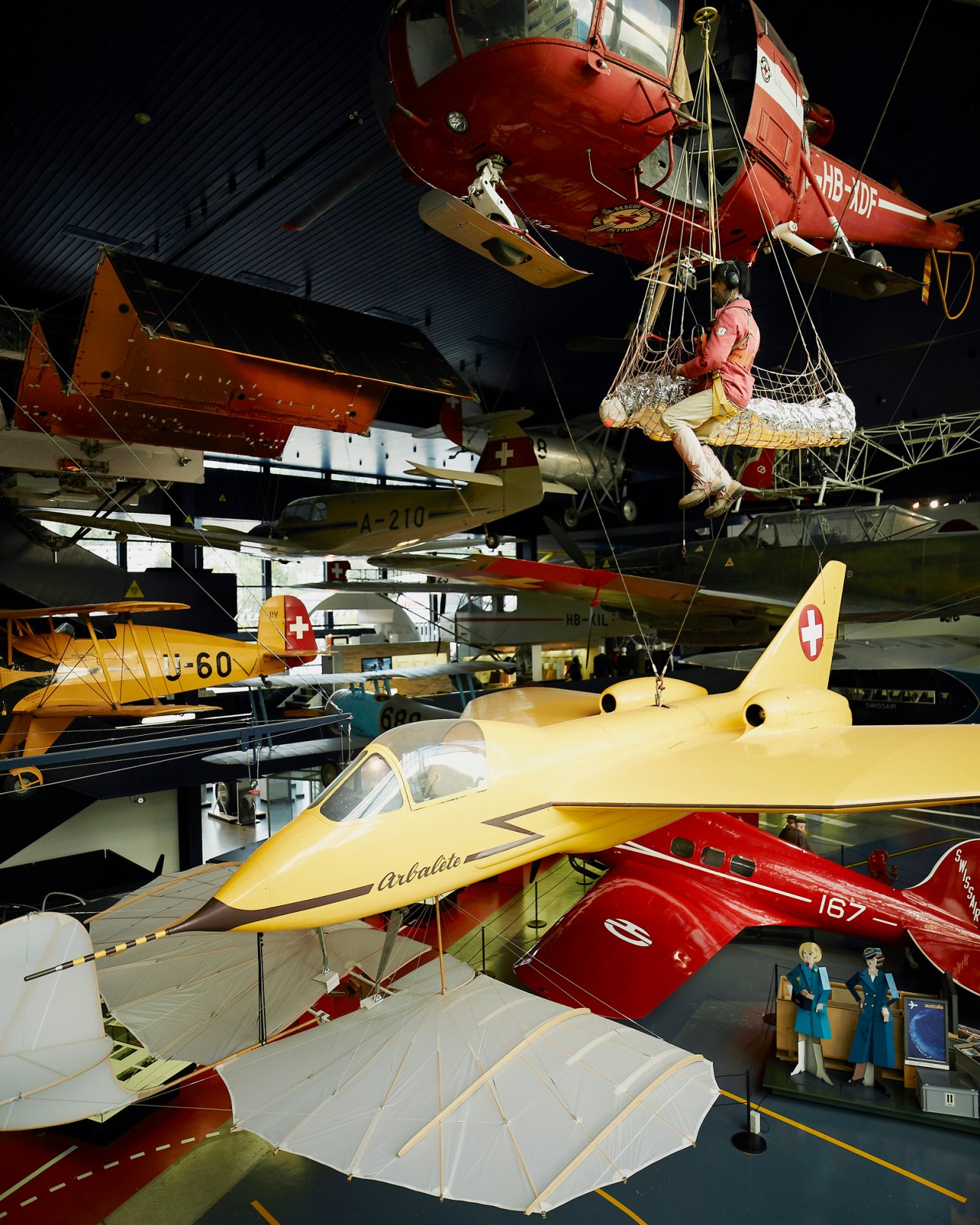 Historic aircraft suspended from ceiling in aviation museum hangar, including red and yellow vintage planes with Swiss markings.