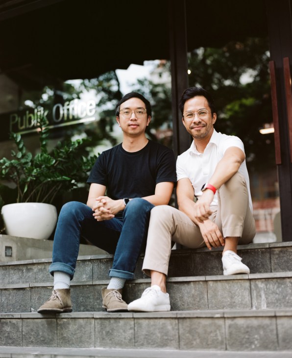 Two men sitting on steps outside a building with a Public Office sign visible behind them.
