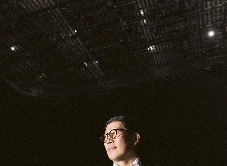 Business executive in glasses and dark suit looking upward against backdrop of urban buildings at night