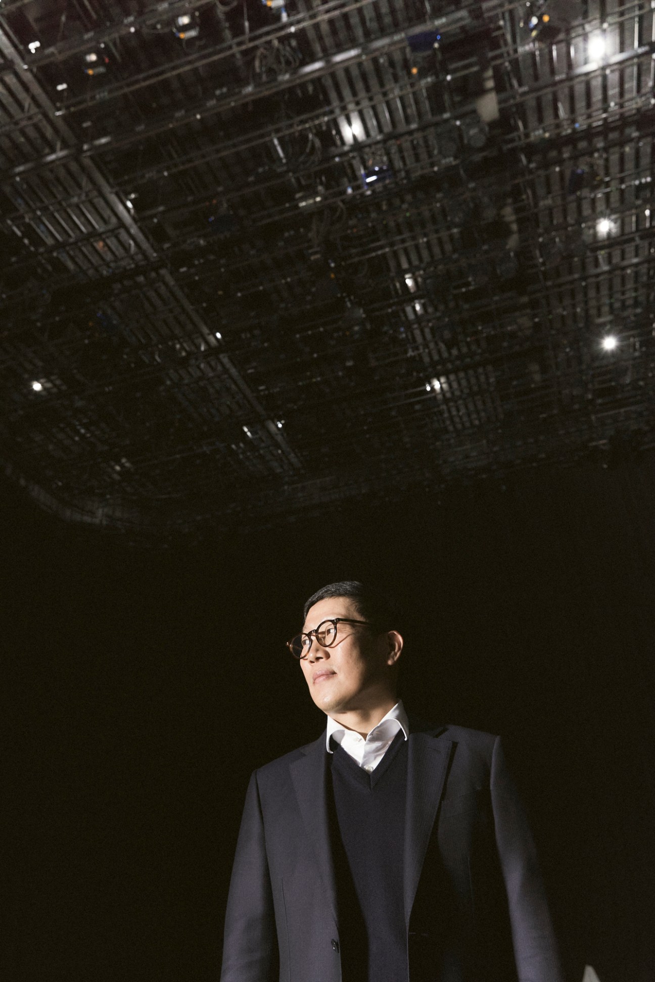 Business executive in glasses and dark suit looking upward against backdrop of urban buildings at night