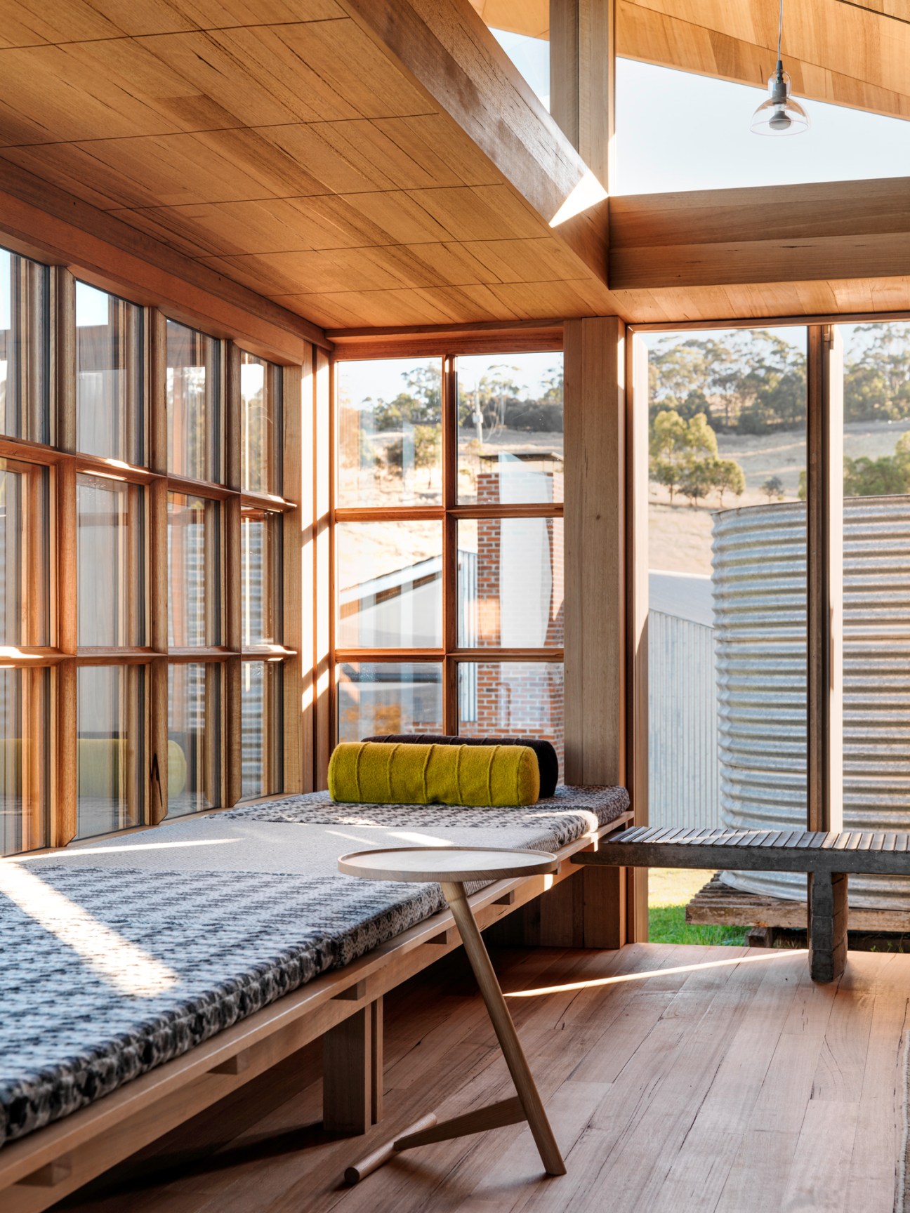 Sunlit interior with wooden ceiling, built-in bench seating, large windows and view of rural landscape