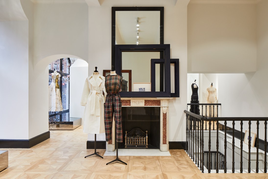 Fashion boutique interior with cream coats on mannequins, fireplace with black frames, and staircase