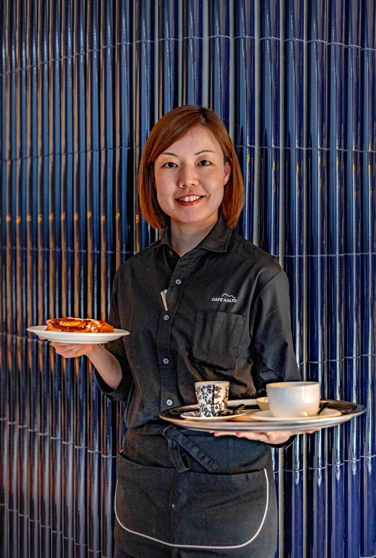 Server at Cafe Aalto holding plates with coffee and pastries in Nordic-designed hotel restaurant