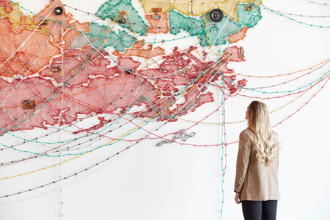 Gallery visitor viewing large colorful textile installation with nets and strings on white wall