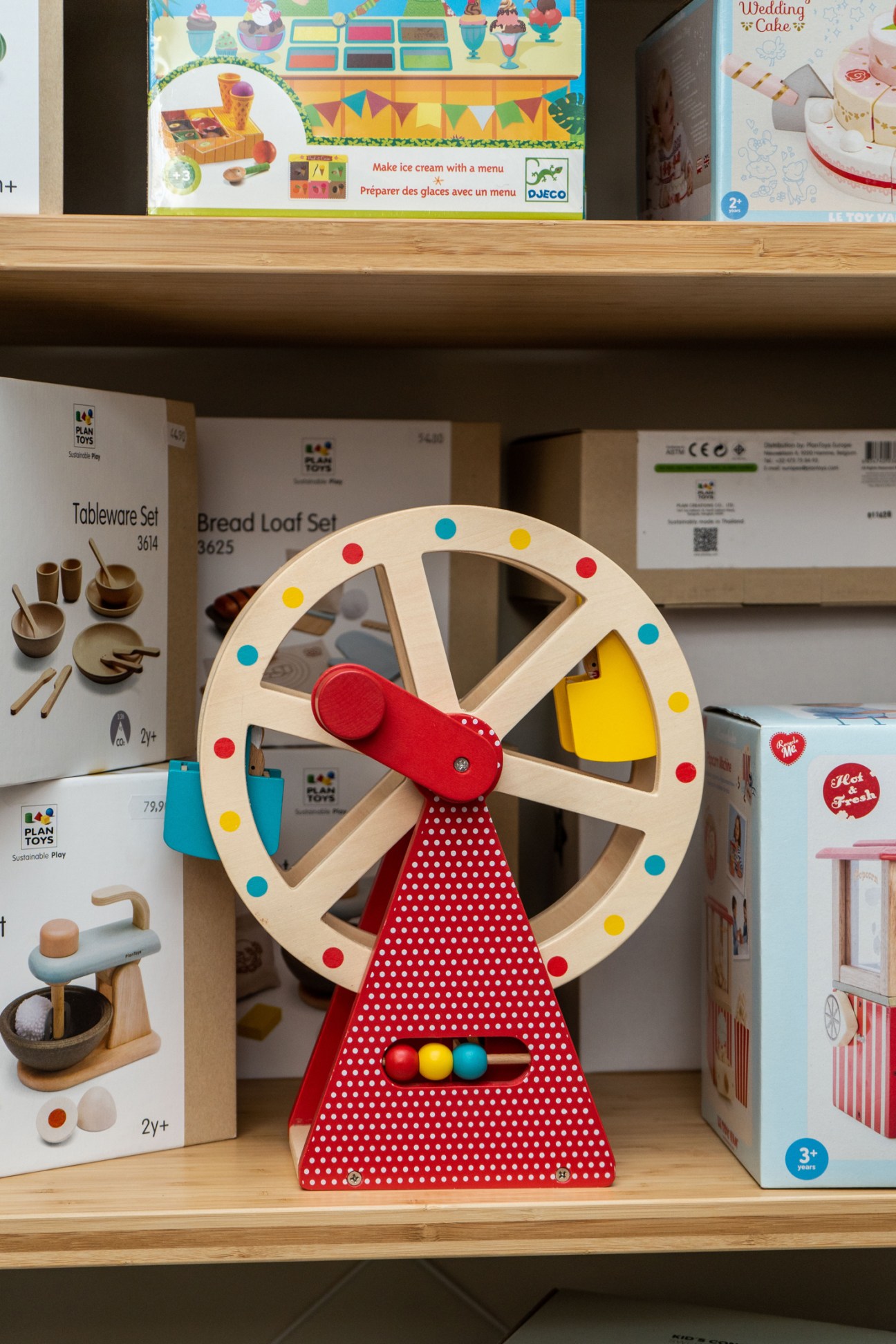 Colorful wooden ferris wheel toy with red polka dot base and yellow and blue cars on display shelf