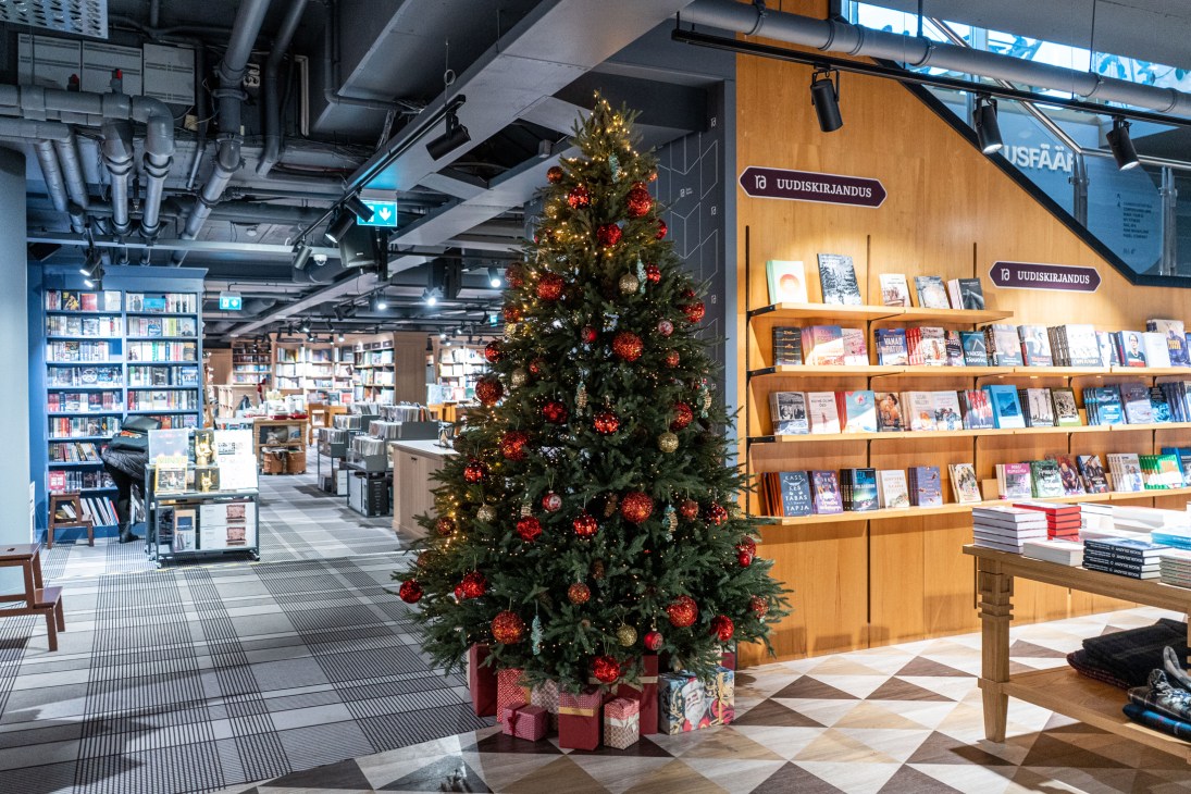 Christmas tree with red and gold ornaments in modern bookstore with wooden shelving and exposed ceiling
