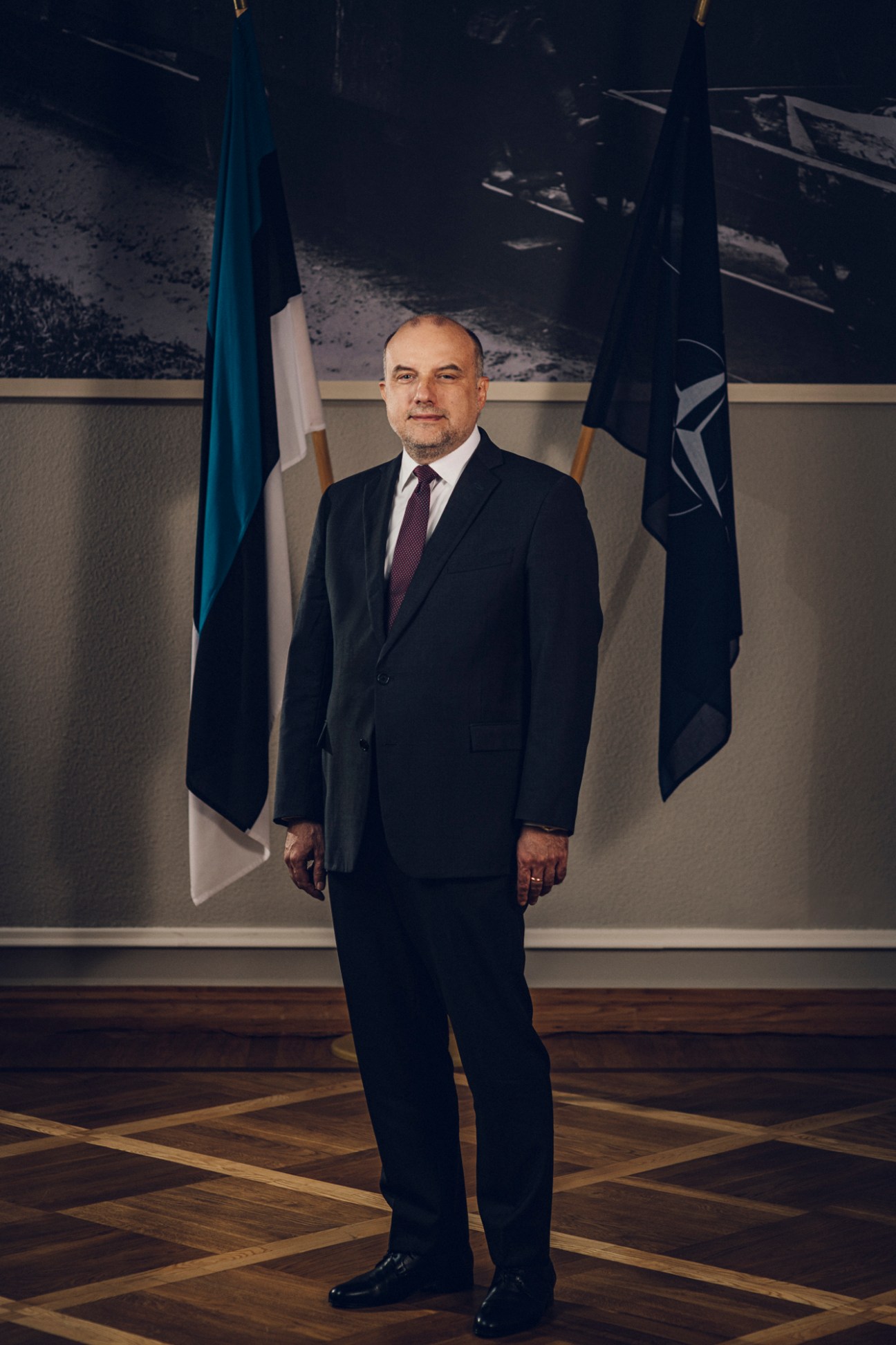Estonian Defence Minister Jüri Luik in formal attire standing before flags in an official government setting