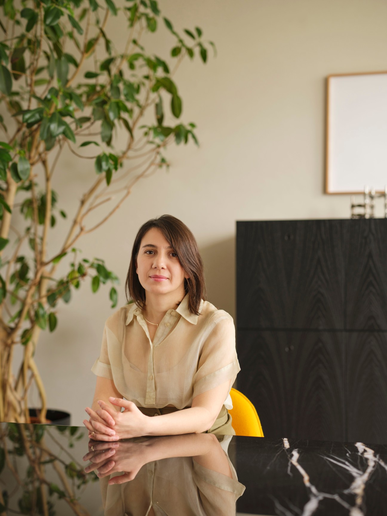 Maria Porro sitting at a reflective table in a modern interior with plants and framed artwork