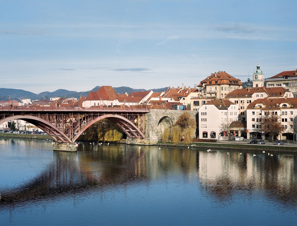 Old bridge across the Drava river with red arches connecting historic buildings in Maribor