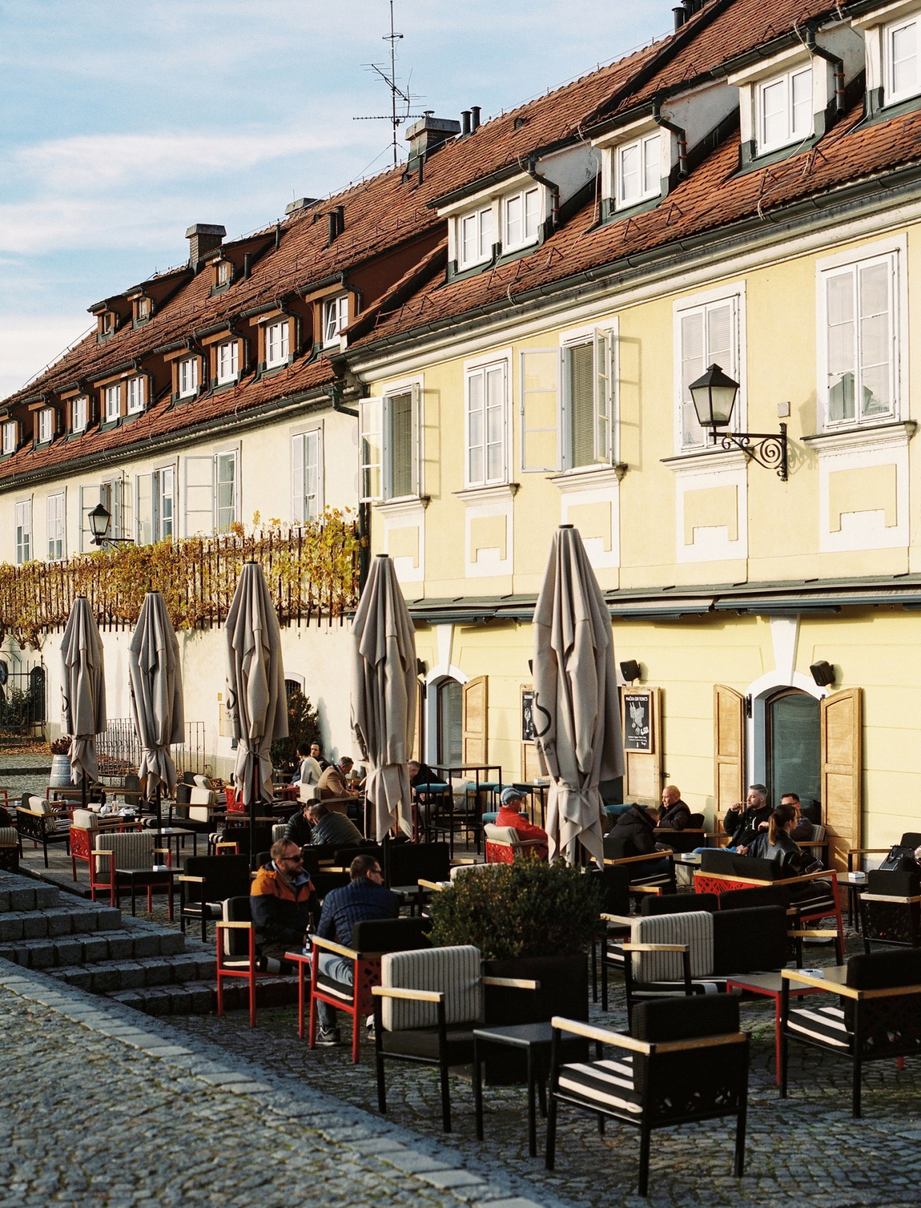 Outdoor cafe terrace with umbrellas and diners seated at tables on cobblestone square surrounded by historic buildings