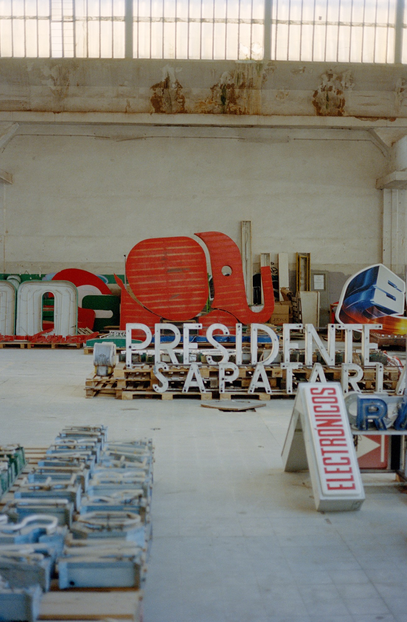 Colorful vintage neon signs and letters stored on wooden pallets in a warehouse with white walls