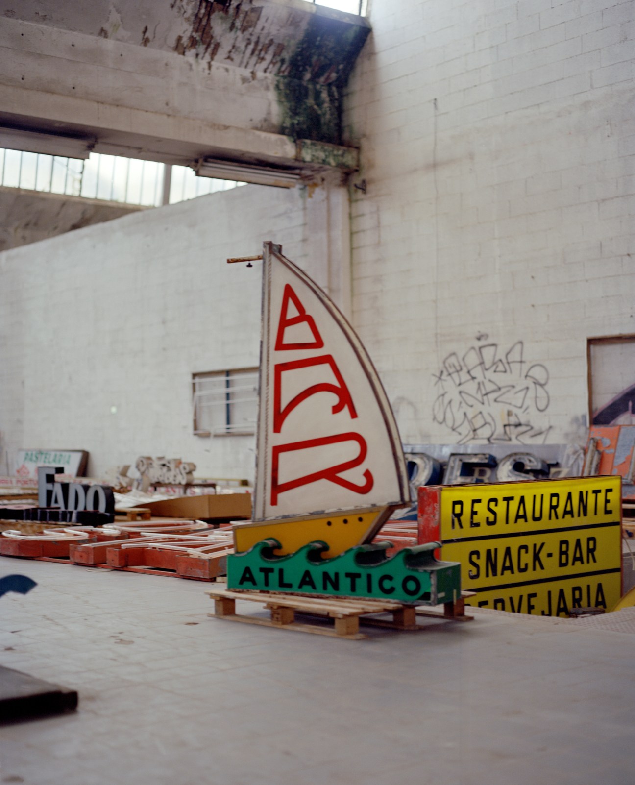 Vintage neon signs including a red sailboat and yellow restaurant snack-bar signs stored in a warehouse
