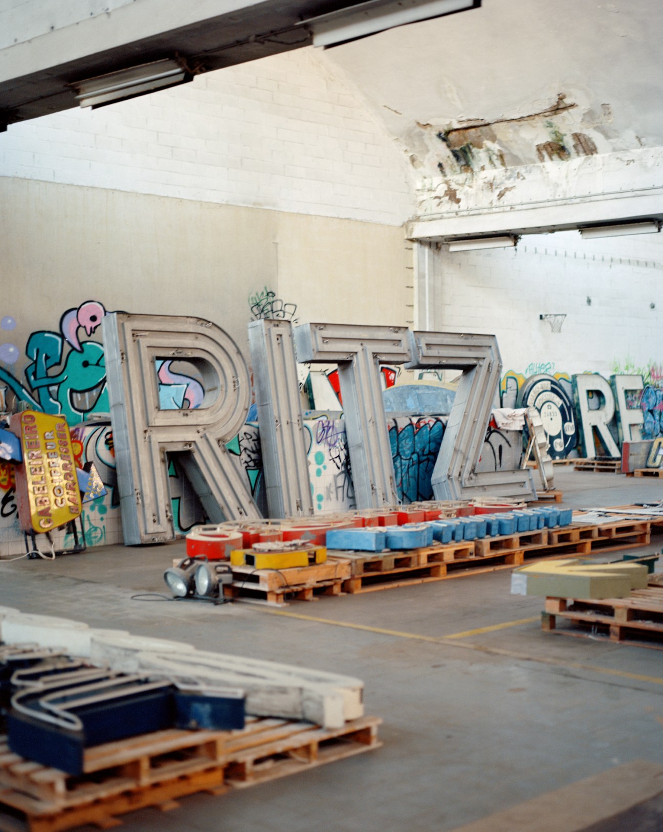 Large metal letters spelling RITZ mounted on wooden pallets in a warehouse with graffitied walls