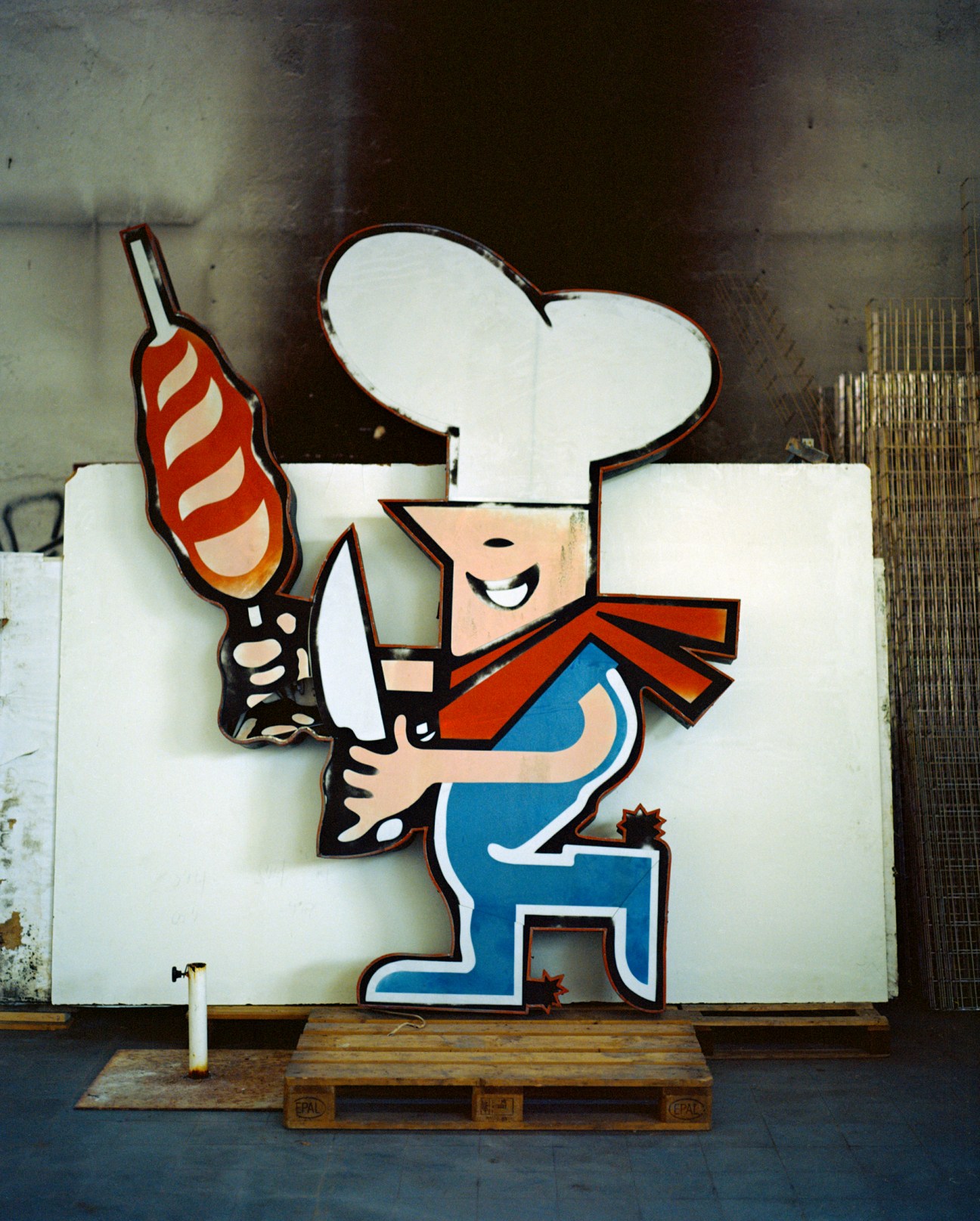 Cartoon chef character sign with white hat, blue apron, and red sausage for Chimarrão Brazilian steakhouse