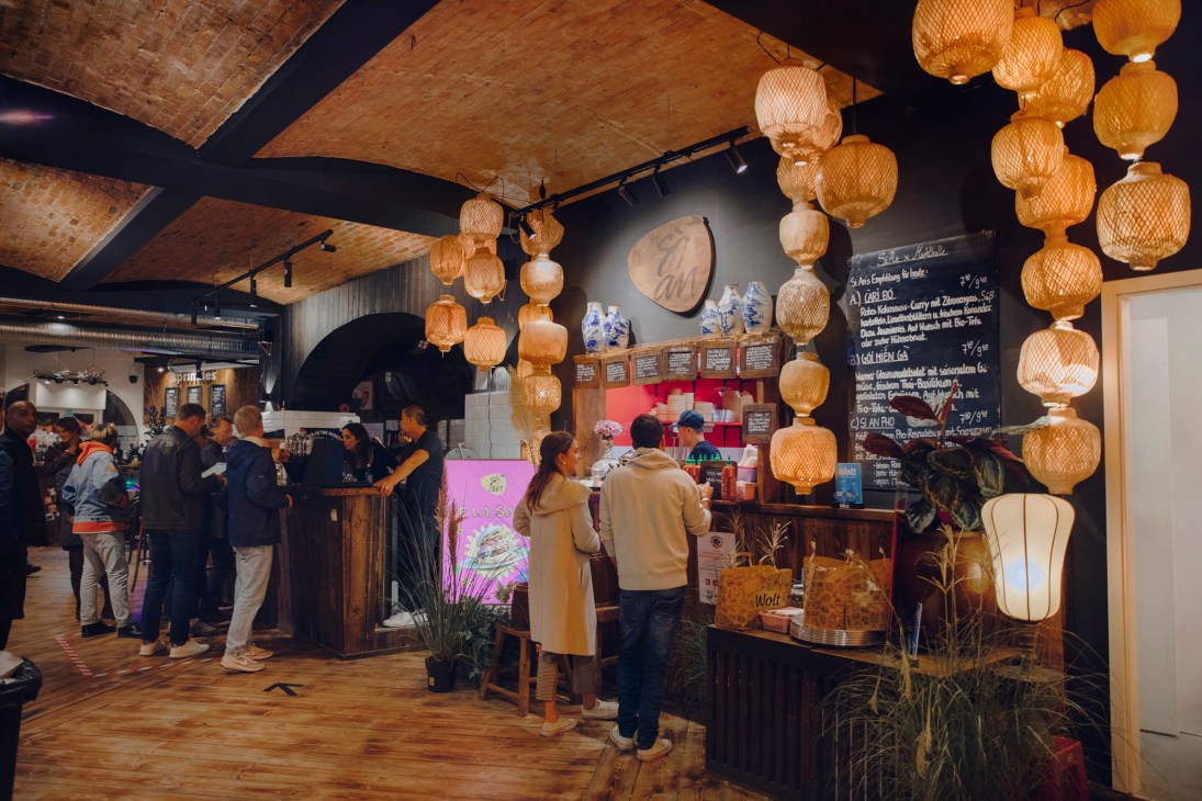 Interior of Markthalle Pfefferberg food hall with woven pendant lights, customers ordering at food stalls, and chalkboard menus