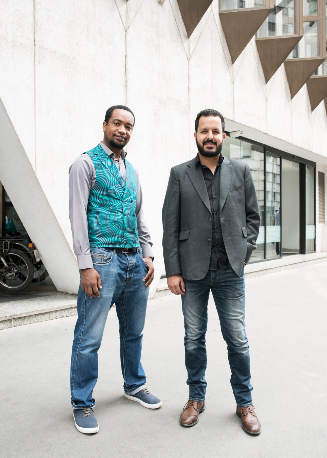 Architects Lahbib El Moumni and Imad Dahmani standing together in front of a modernist concrete building.