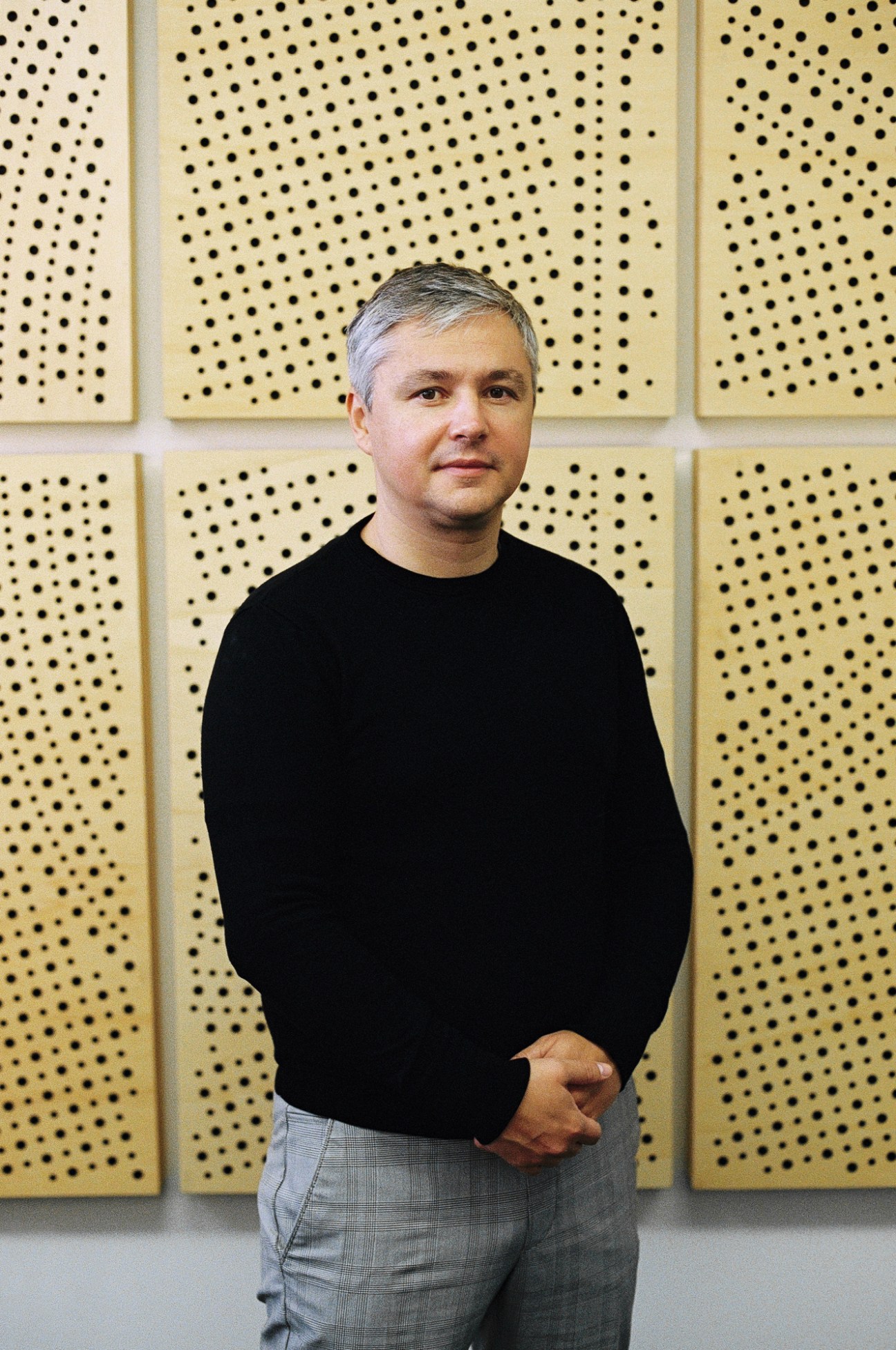 Matej Hotko stands against a perforated wood acoustic panel wall wearing a black sweater