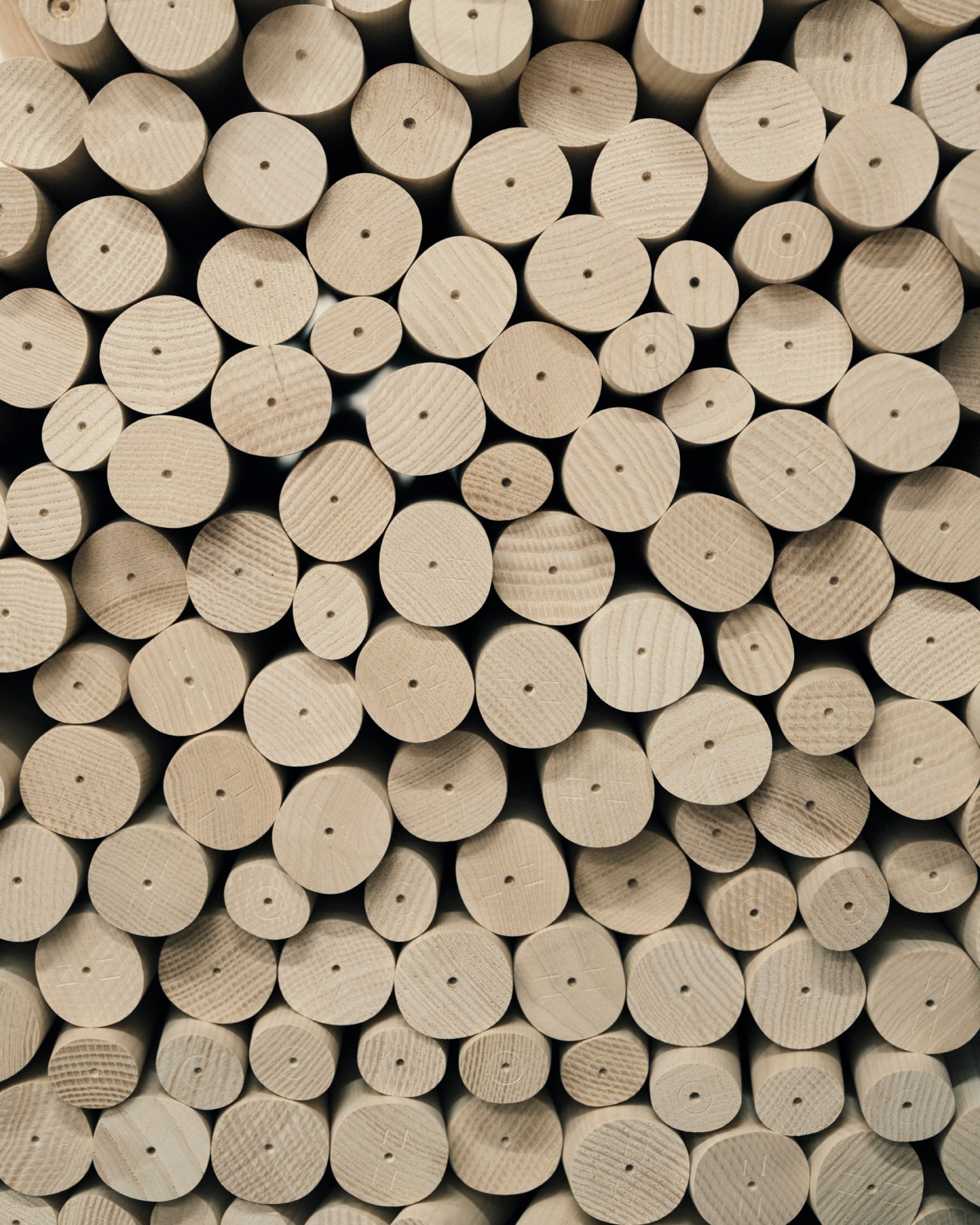 Circular wooden dowels of varying sizes arranged closely together, each with a small drilled hole in the center