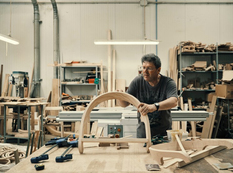 Craftsman Walter Vogrig working on a curved wooden chair component in the Mattiazzi factory workshop