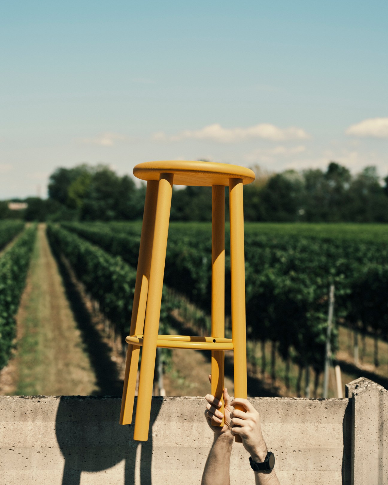 Solo Stool by Nitzan Cohen held by hands against a vineyard landscape background