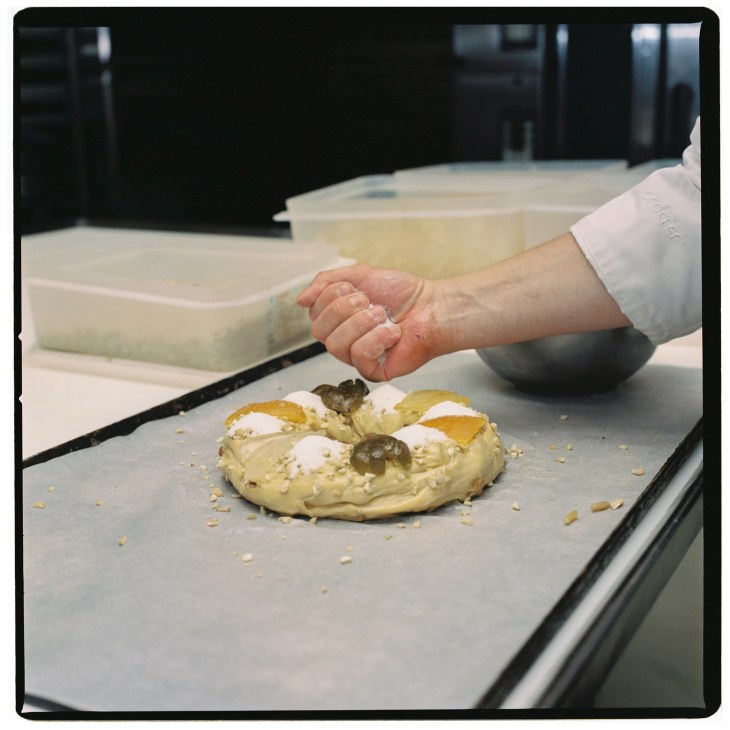 Baker's hand decorating a Portuguese bolo rei king cake with candied fruit and nuts.