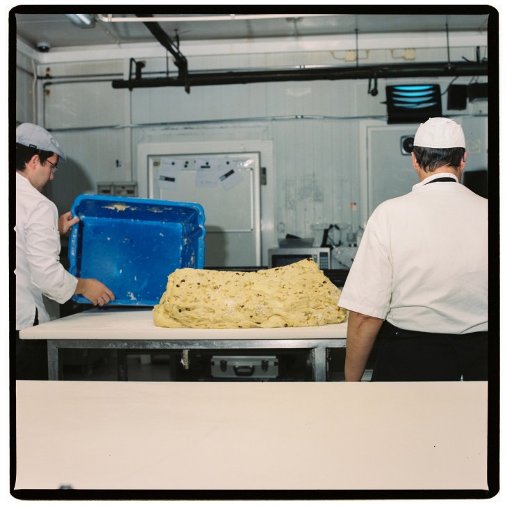Two bakers in white uniforms and hairnets working with dough at Confeitaria Nacional in Lisbon.