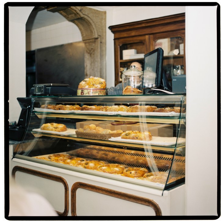 Display case at Confeitaria Nacional pastry shop showing bolo rei cakes and other pastries behind glass.