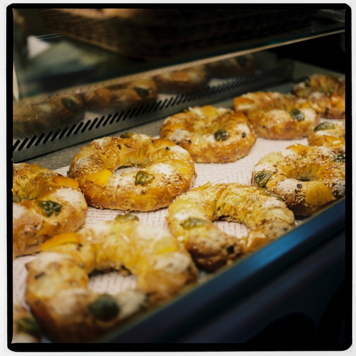 Freshly baked Portuguese bolo rei king cakes with candied fruit and nuts on a conveyor belt.