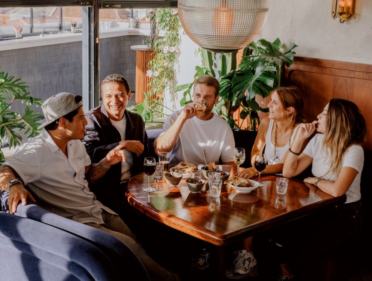 Five people dining together at wooden table in restaurant with plants and pendant lighting