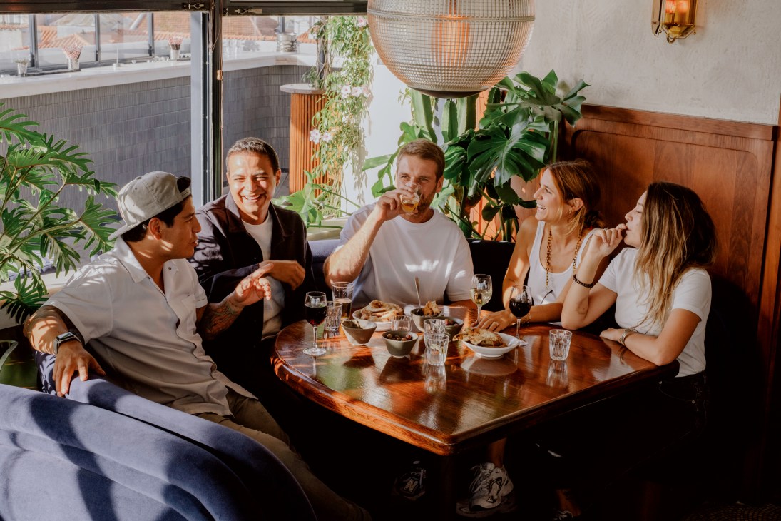Five people dining together at wooden table in restaurant with plants and pendant lighting