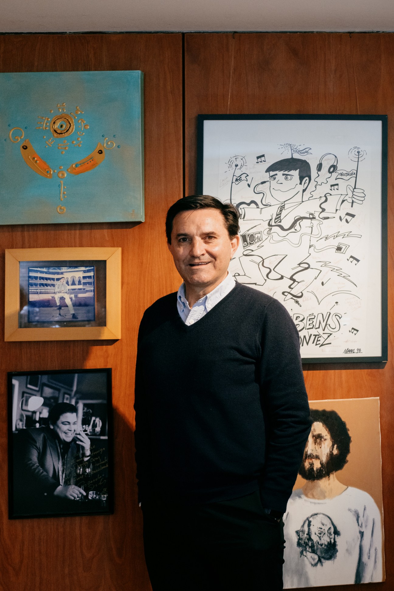 Luis Montez stands in front of wood-paneled wall with framed artwork and photographs displayed behind him.