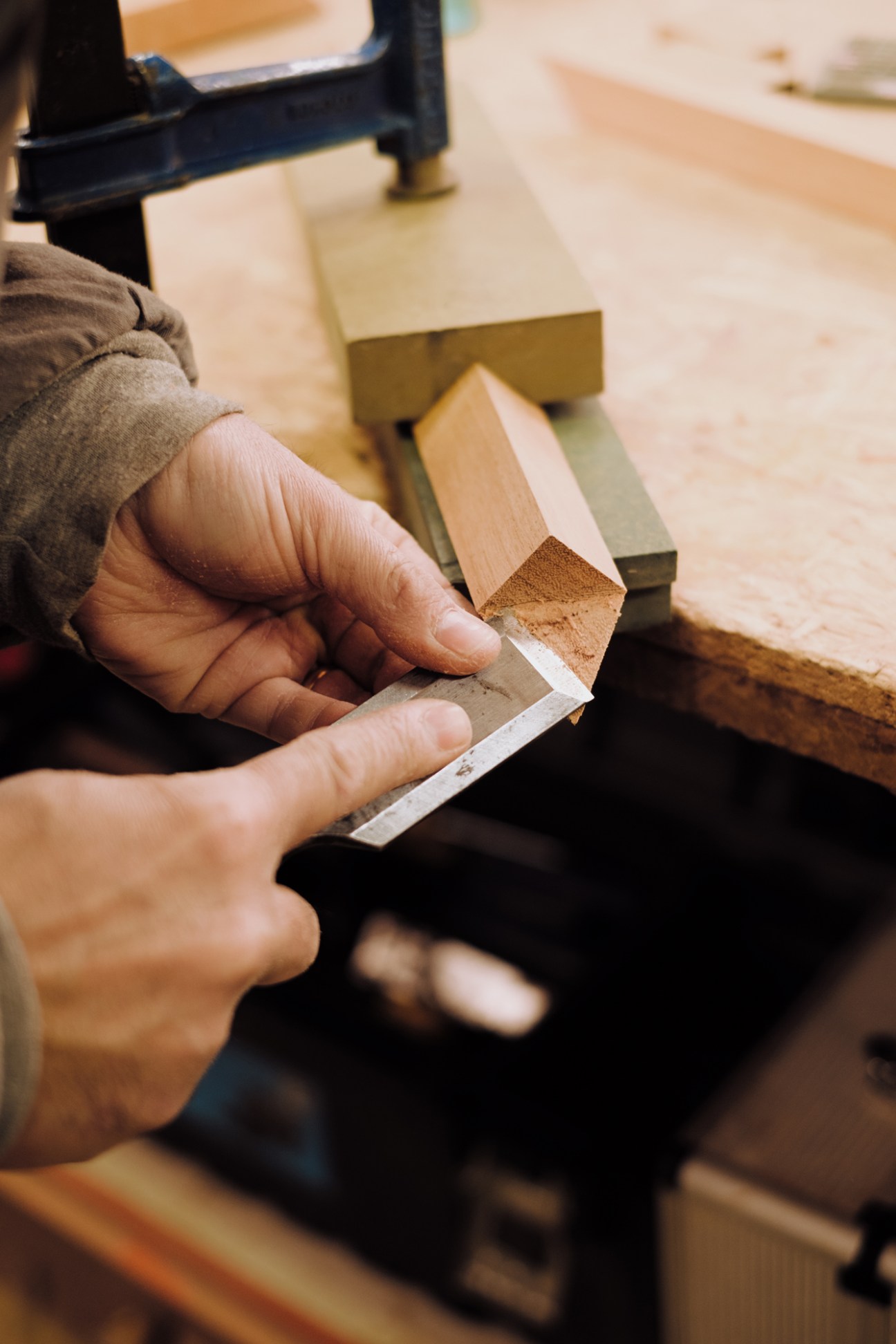 Hands using chisel on wood piece in carpentry workshop showing traditional woodworking craftsmanship