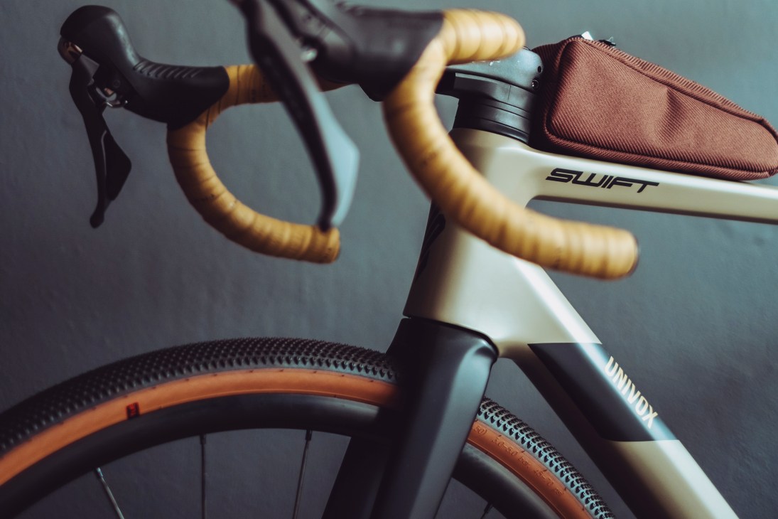 Close-up of a Swift bicycle showing cream-colored frame, tan leather handlebars, and orange-sidewall tire