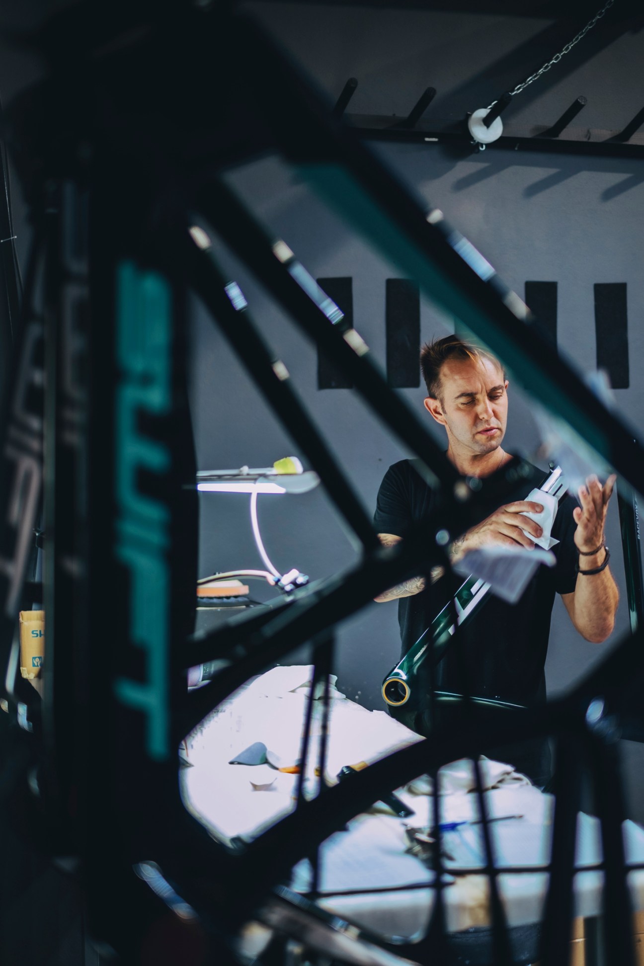 Worker at Incycles factory in a black shirt, inspecting bicycle frame components in an industrial factory setting with metal framework handling bicycle frame transformation process
