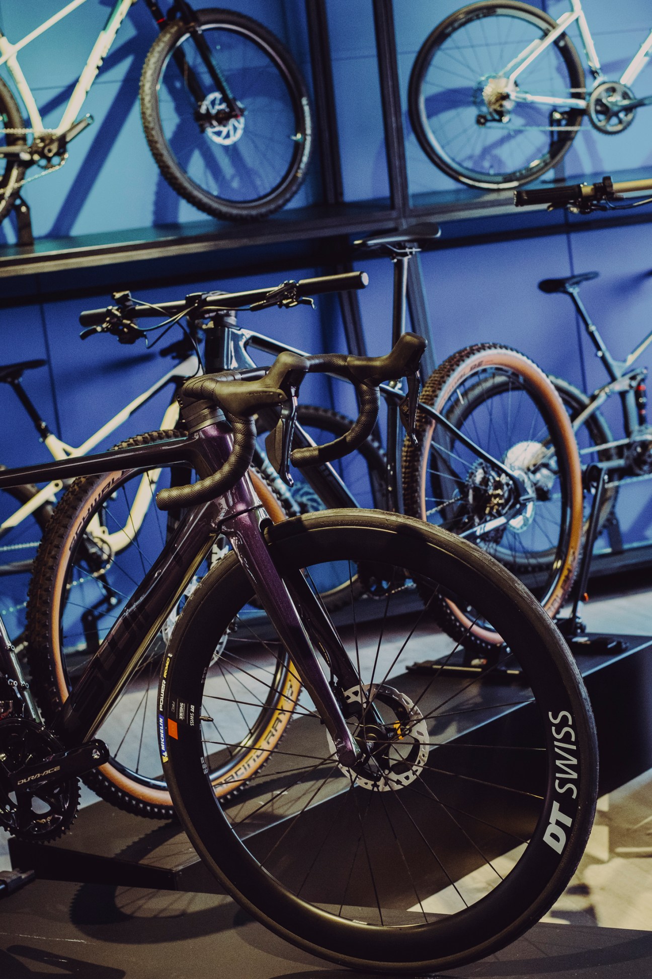 High-end bicycles displayed in a modern showroom with purple lighting and bike wheels visible on upper shelves. Interior view of Swift Carbon's modern showroom in Porto featuring displayed bicycles and a clean, minimal design