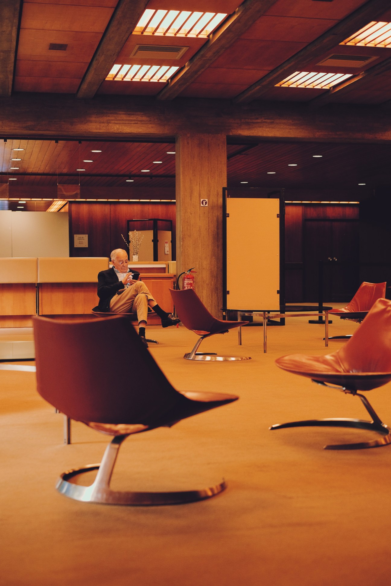 Man in business attire sitting alone in a mid-century modern interior with orange and red furniture