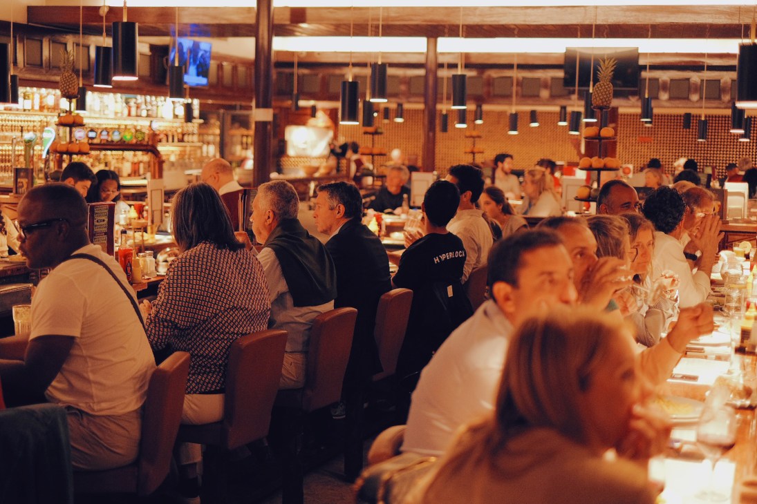 People seated at a counter in a busy restaurant or diner with warm lighting and wooden interior