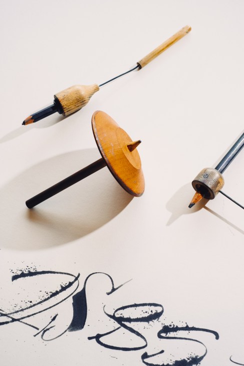 Three wooden calligraphy tools with metal nibs arranged on white surface with black ink strokes below