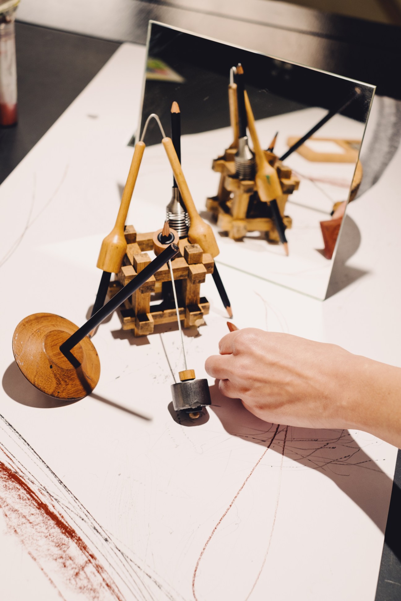 Wooden drawing contraption with compass-like arms and weighted mechanism being tested on white paper