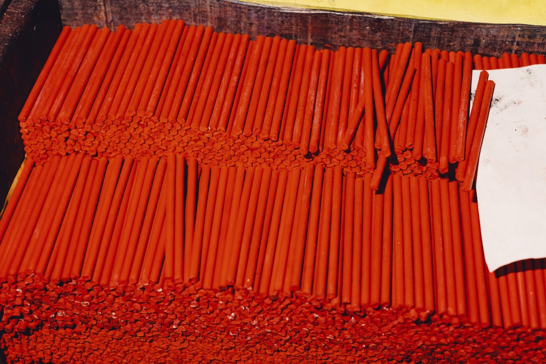 Hundreds of bright orange colored pencil cores arranged in neat rows on a wooden surface