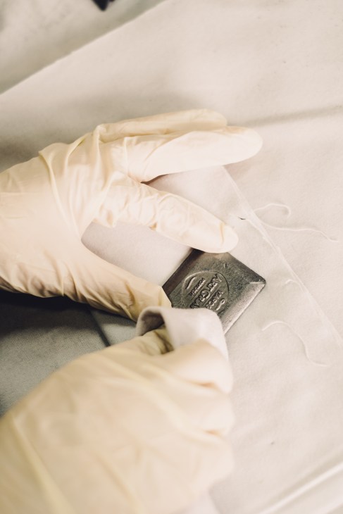Hands in white gloves polishing a dark rectangular graphite block on white fabric