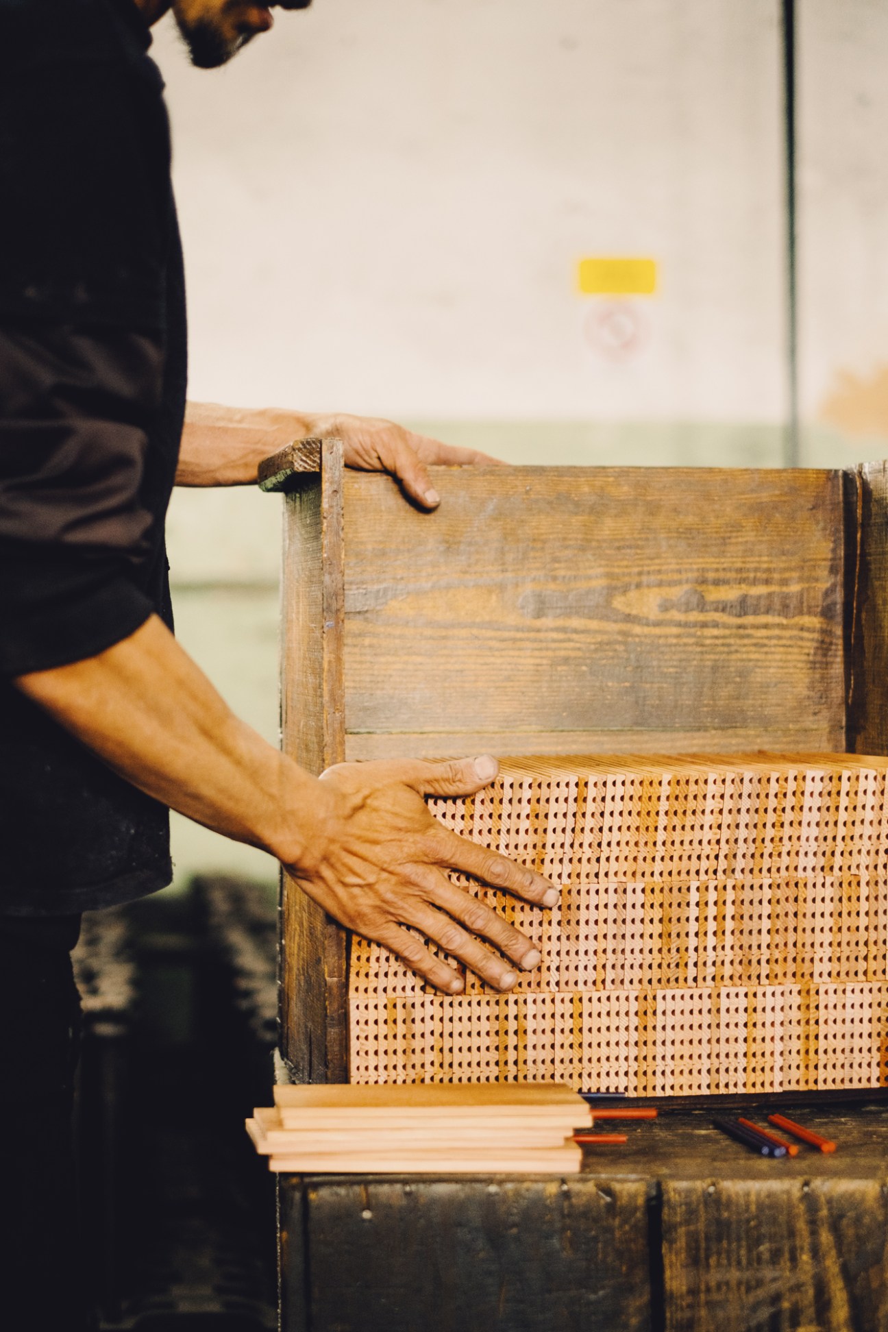 Hands positioning wooden slats with woven cane material on a workbench during pencil manufacturing