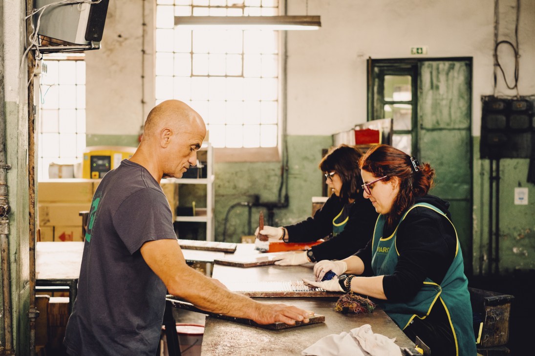 Factory employees glue pencil cores to wood slats in industrial workshop setting