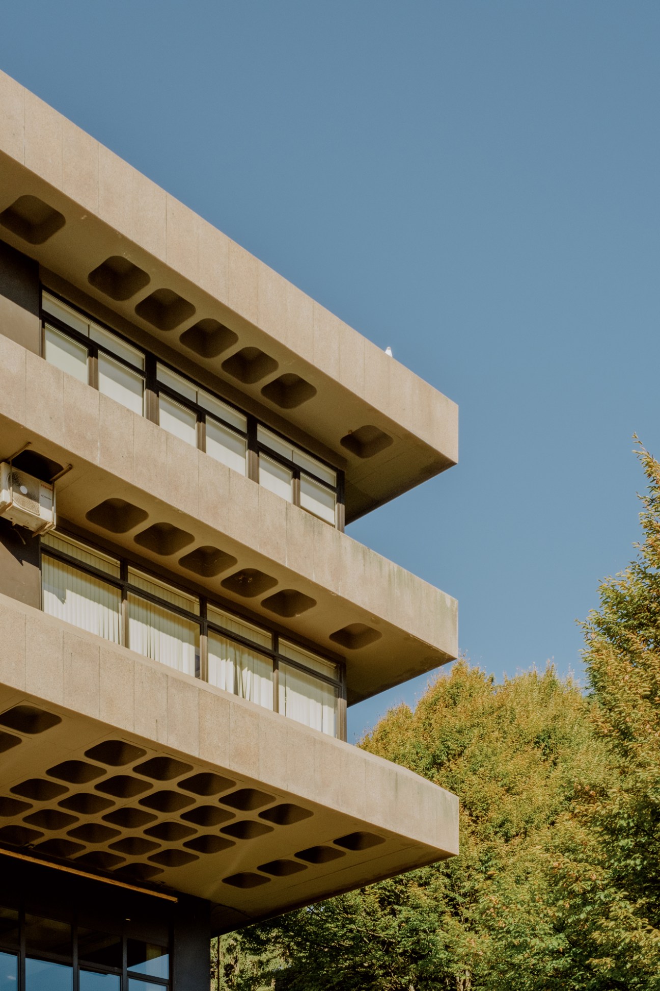 Modern concrete building with geometric cantilever balconies and hexagonal ceiling perforations under blue sky