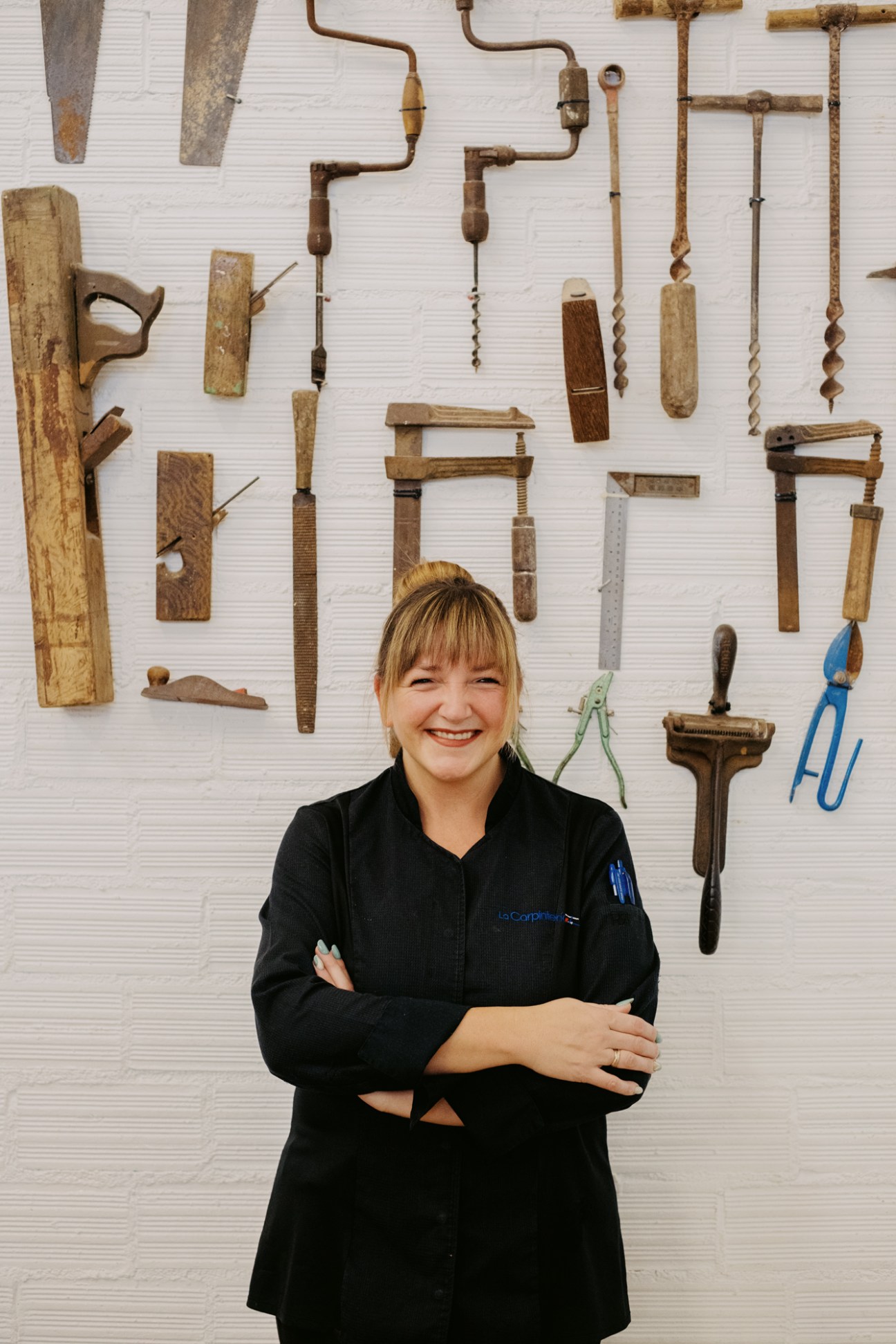 Elena Garmendia from La Carpintería restaurant standing with crossed arms in front of wall displaying vintage woodworking tools