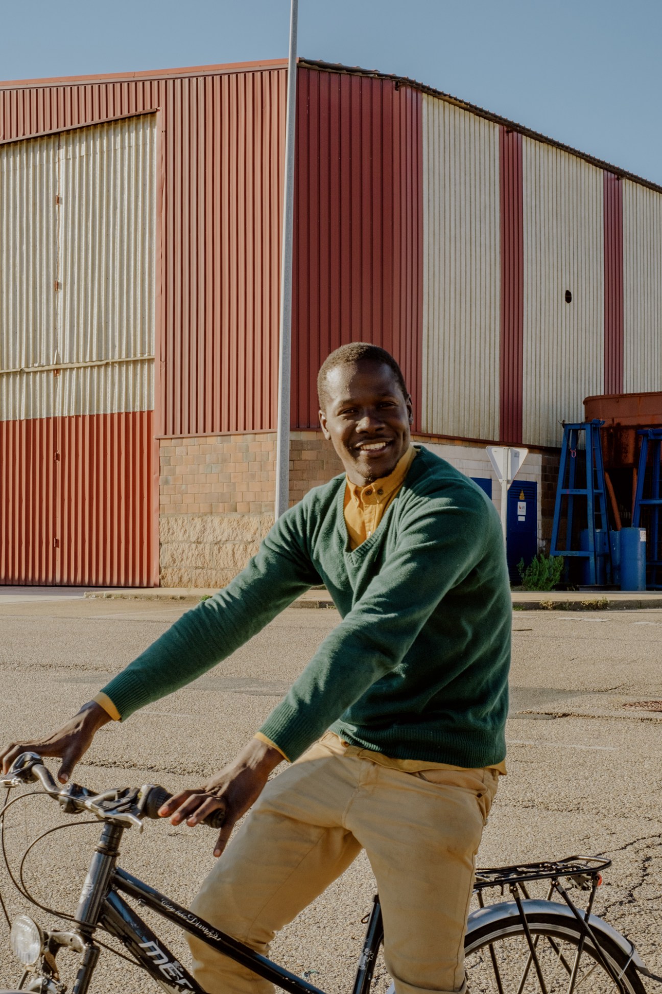Man in green sweater riding bicycle near industrial port buildings in Vigo
