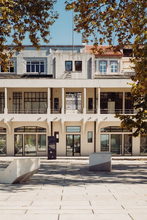 Modernist building facade with cream-colored storefronts and autumn foliage framing the plaza in Guimarães.
