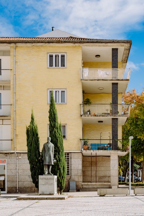 Yellow brick mid-century apartment building with balconies and a statue in foreground in Guimarães.